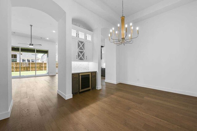 unfurnished living room featuring ceiling fan with notable chandelier, wine cooler, and dark hardwood / wood-style flooring