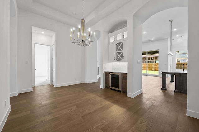 unfurnished living room featuring a notable chandelier, beverage cooler, dark wood-type flooring, and sink