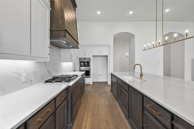 kitchen with custom exhaust hood, hanging light fixtures, sink, dark wood-type flooring, and white cabinetry