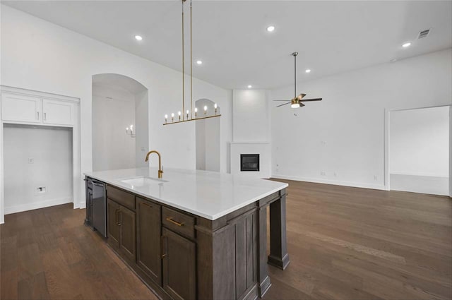 kitchen featuring ceiling fan with notable chandelier, dark hardwood / wood-style flooring, a large fireplace, a center island with sink, and sink