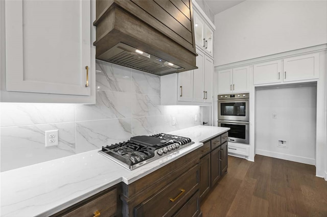 kitchen with tasteful backsplash, white cabinetry, custom range hood, appliances with stainless steel finishes, and dark hardwood / wood-style flooring