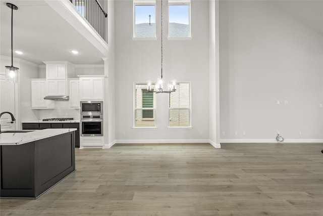 kitchen featuring light stone counters, stainless steel appliances, sink, decorative light fixtures, and white cabinetry