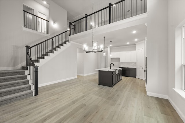 kitchen with a high ceiling, white cabinets, hanging light fixtures, sink, and an island with sink