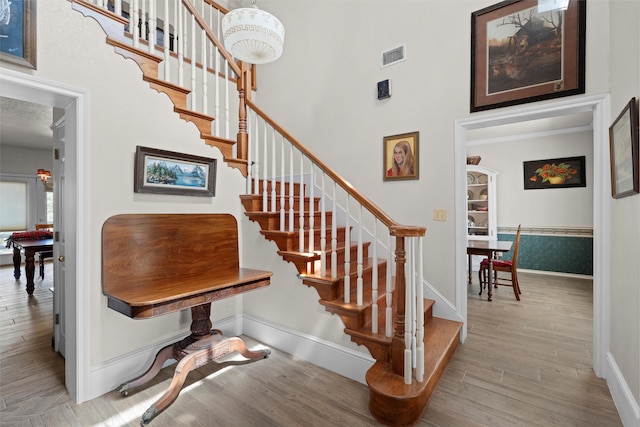 stairway featuring a towering ceiling, hardwood / wood-style floors, and a chandelier