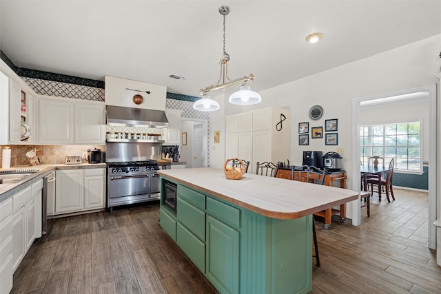 kitchen featuring stainless steel appliances, a breakfast bar, wall chimney range hood, a center island, and white cabinetry