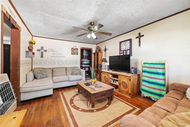 living room featuring a ceiling fan, a textured ceiling, ornamental molding, and wood finished floors