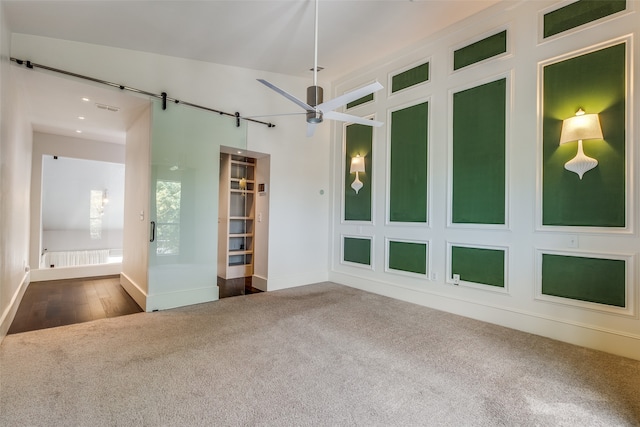 carpeted empty room featuring a barn door and ceiling fan