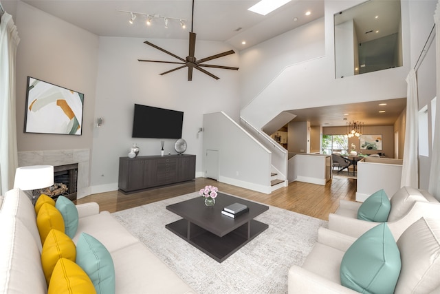 living room featuring high vaulted ceiling, ceiling fan with notable chandelier, hardwood / wood-style floors, and a premium fireplace