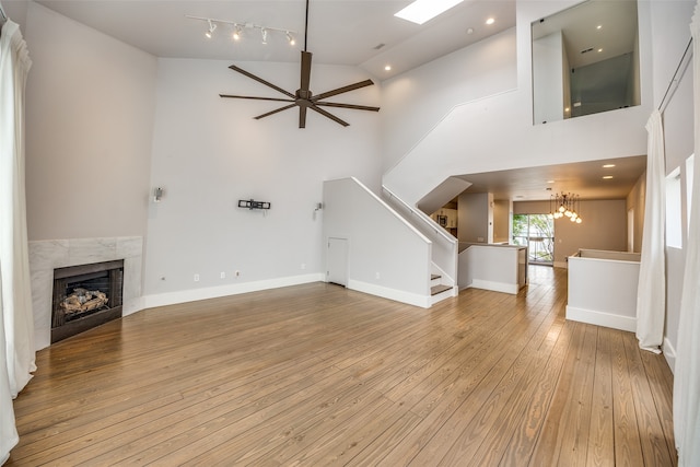 unfurnished living room with ceiling fan with notable chandelier, light wood-type flooring, and high vaulted ceiling