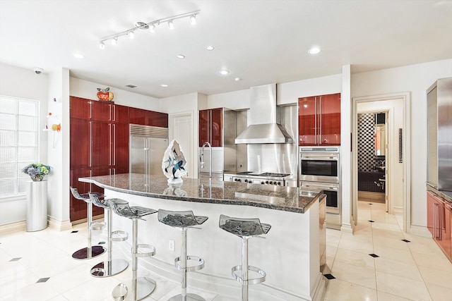 kitchen with a large island, appliances with stainless steel finishes, a breakfast bar, dark stone countertops, and wall chimney exhaust hood