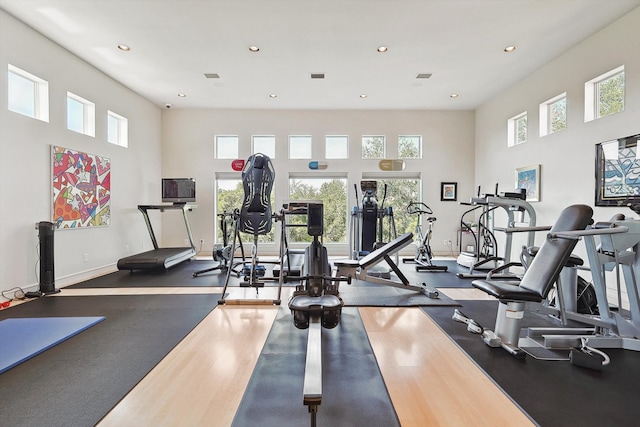 gym with a towering ceiling, dark hardwood / wood-style floors, and a wealth of natural light