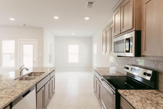 kitchen with light stone countertops, stainless steel appliances, light tile patterned floors, backsplash, and sink