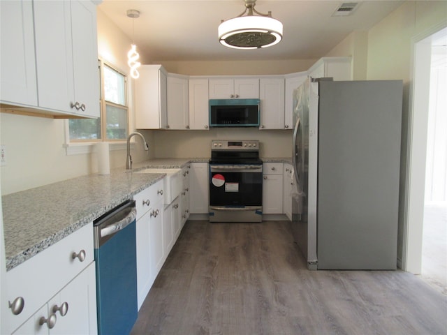 kitchen with sink, light stone countertops, appliances with stainless steel finishes, decorative light fixtures, and white cabinetry