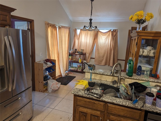 kitchen with vaulted ceiling, light tile patterned floors, pendant lighting, stone countertops, and stainless steel fridge with ice dispenser