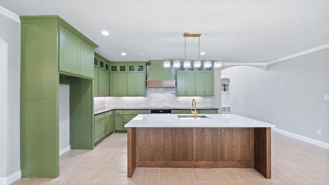 kitchen featuring tasteful backsplash, a center island with sink, sink, premium range hood, and ornamental molding