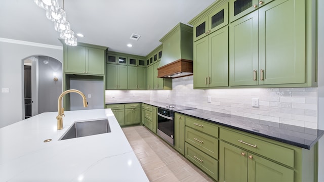 kitchen featuring tasteful backsplash, premium range hood, decorative light fixtures, oven, and green cabinets