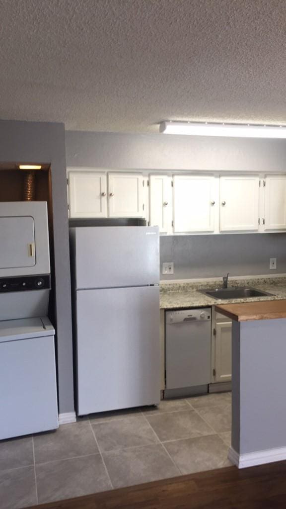 kitchen featuring white appliances, white cabinets, sink, a textured ceiling, and stacked washer / drying machine