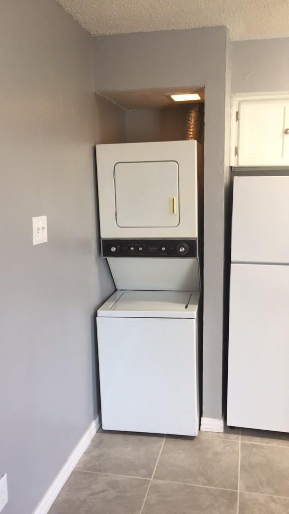 laundry room with light tile patterned floors, a textured ceiling, and stacked washer and clothes dryer