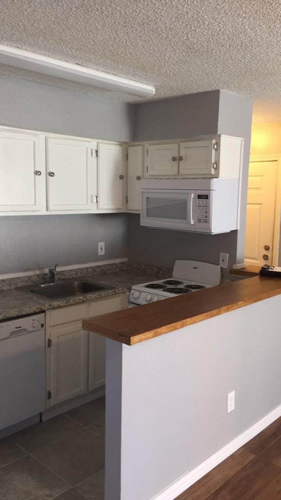 kitchen featuring sink, dark tile patterned floors, kitchen peninsula, white appliances, and white cabinets