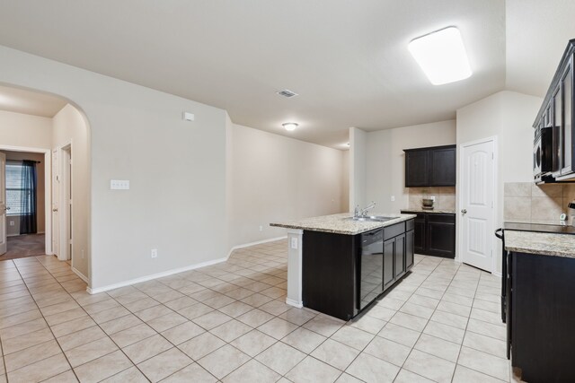 kitchen featuring a center island with sink, backsplash, light stone countertops, light tile patterned flooring, and dishwasher