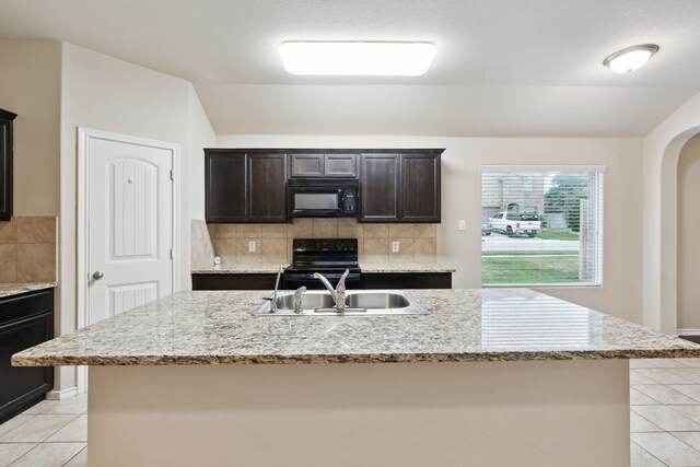 kitchen with range, decorative backsplash, an island with sink, sink, and light tile patterned floors