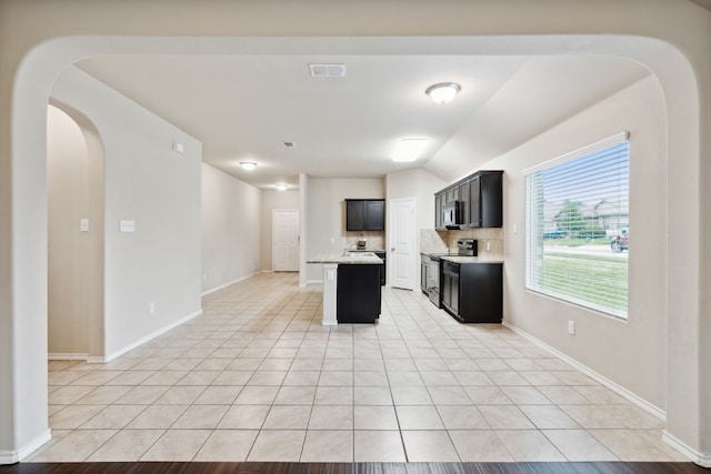 kitchen featuring decorative backsplash, electric stove, a center island with sink, and light tile patterned floors