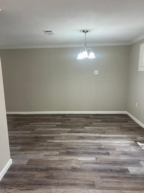 empty room featuring an inviting chandelier, dark hardwood / wood-style floors, and ornamental molding