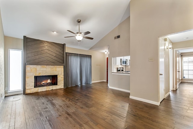 unfurnished living room featuring ceiling fan, a stone fireplace, high vaulted ceiling, and dark wood-type flooring