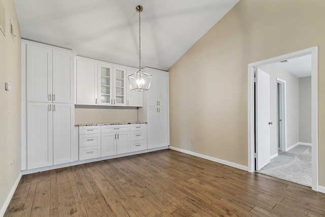 unfurnished dining area with a notable chandelier, carpet flooring, and high vaulted ceiling