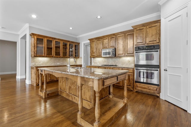 kitchen featuring a center island with sink, a kitchen breakfast bar, sink, light stone countertops, and appliances with stainless steel finishes