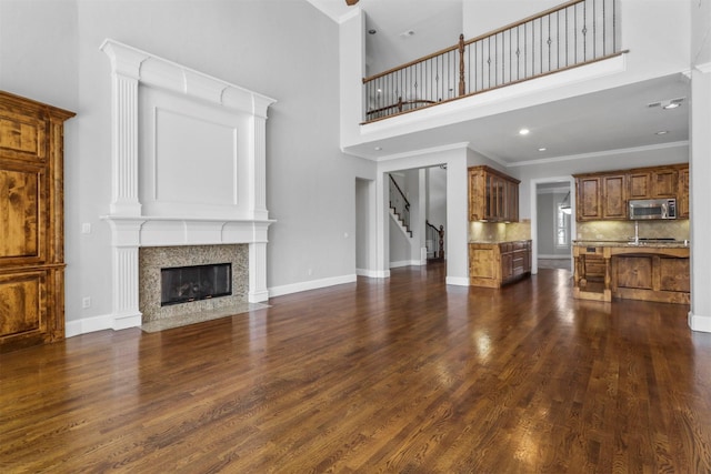 unfurnished living room with a premium fireplace, dark wood-type flooring, a high ceiling, and ornamental molding