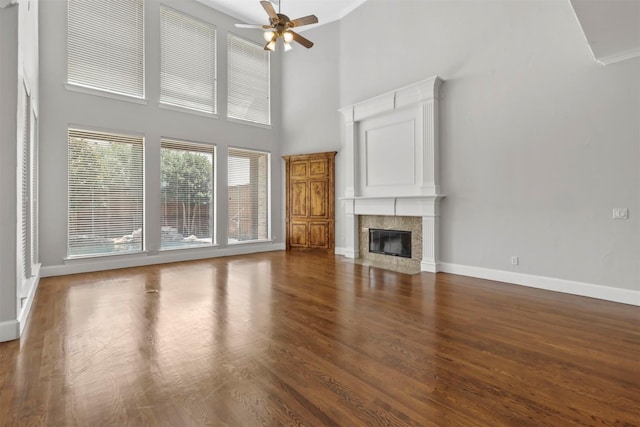 unfurnished living room with dark hardwood / wood-style flooring, ceiling fan, a fireplace, and a towering ceiling