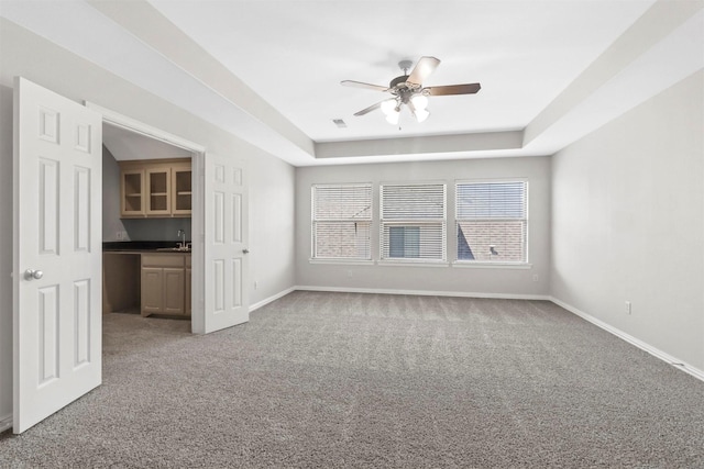 unfurnished living room featuring a tray ceiling, ceiling fan, sink, and carpet floors