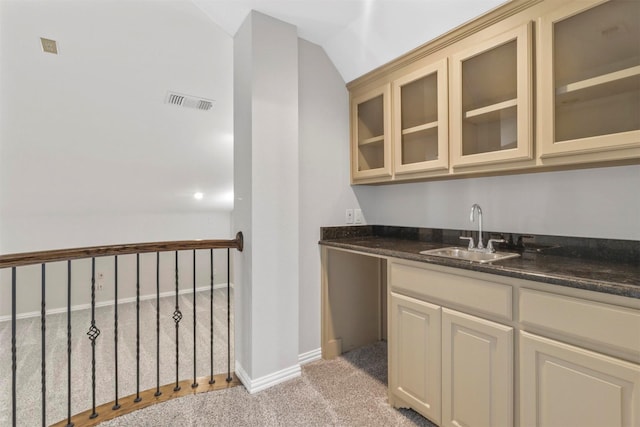 kitchen featuring light carpet, dark stone counters, vaulted ceiling, sink, and cream cabinetry