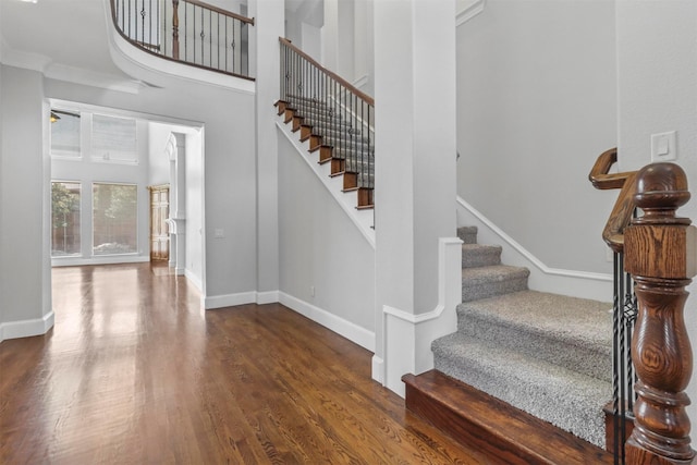 staircase featuring a high ceiling, hardwood / wood-style flooring, and crown molding