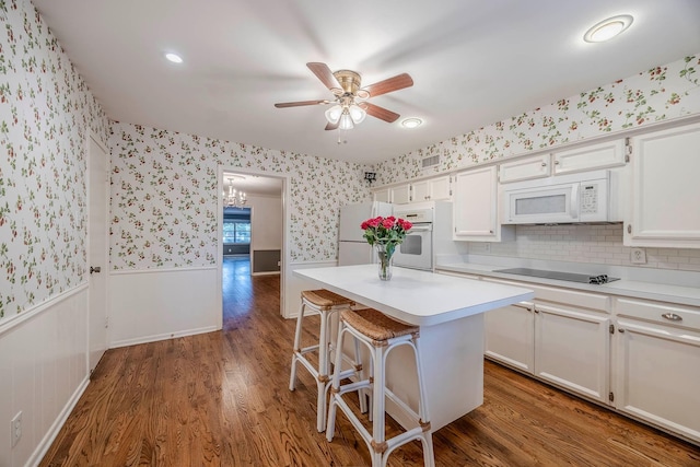 kitchen with a kitchen bar, white appliances, white cabinetry, and a kitchen island