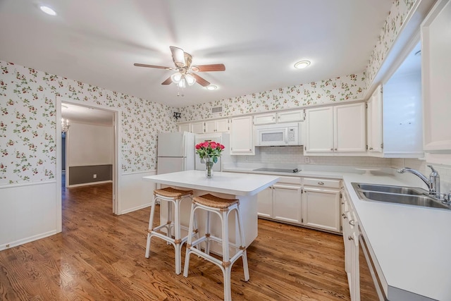 kitchen featuring a center island, a kitchen bar, sink, white appliances, and white cabinetry