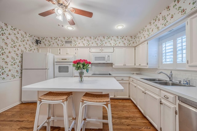 kitchen featuring white cabinetry, light hardwood / wood-style floors, a breakfast bar area, white appliances, and sink