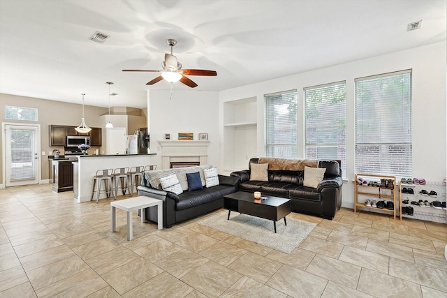 tiled living room featuring built in shelves and ceiling fan