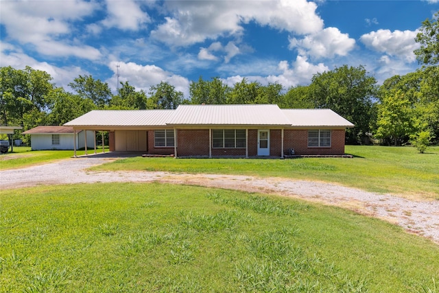 ranch-style house featuring metal roof, an attached carport, brick siding, driveway, and a front lawn