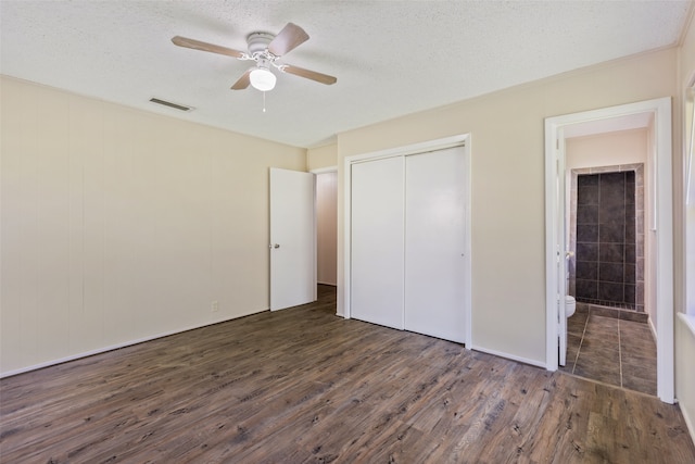 unfurnished bedroom with a closet, ceiling fan, dark hardwood / wood-style floors, ensuite bathroom, and a textured ceiling