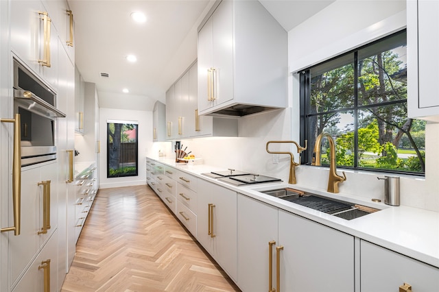 kitchen with light parquet flooring, white cabinetry, a healthy amount of sunlight, and stainless steel oven