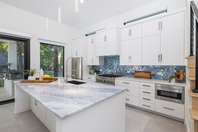 kitchen featuring appliances with stainless steel finishes, a kitchen island with sink, hanging light fixtures, sink, and white cabinetry