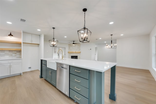 kitchen with an island with sink, ceiling fan, a fireplace, stainless steel dishwasher, and sink