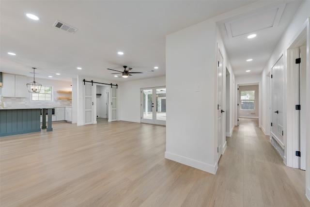 living room featuring ceiling fan with notable chandelier, a barn door, and light wood-type flooring