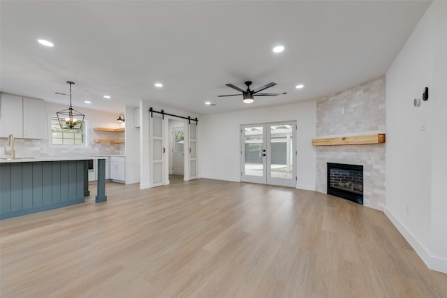 unfurnished living room featuring a barn door, light hardwood / wood-style floors, ceiling fan, a large fireplace, and sink