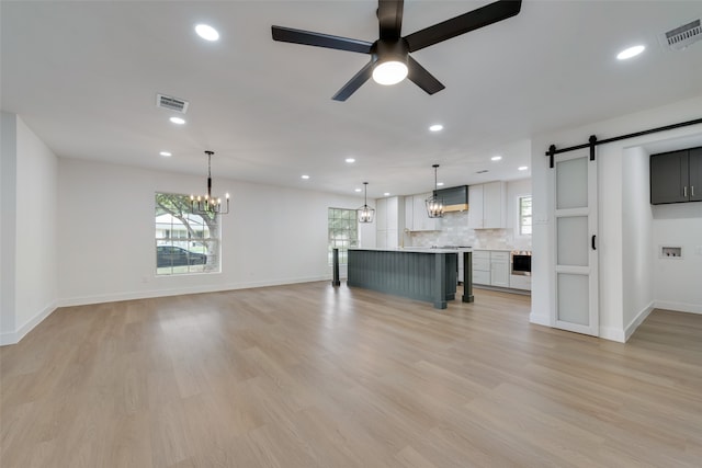 unfurnished living room featuring ceiling fan with notable chandelier, light hardwood / wood-style floors, and a barn door