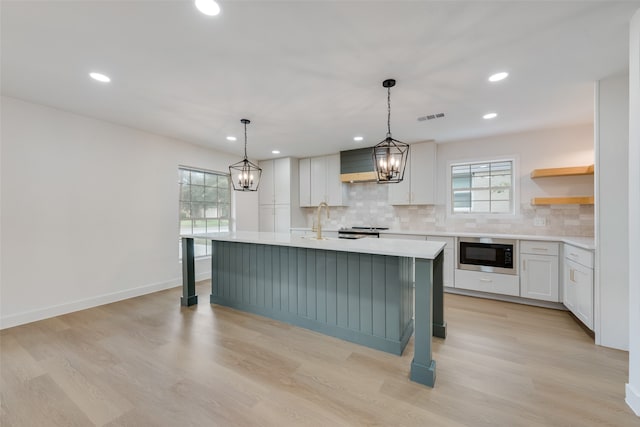 kitchen with white cabinets, a center island, hanging light fixtures, light hardwood / wood-style flooring, and built in microwave