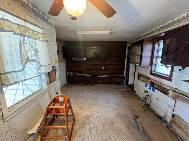 living room featuring ceiling fan, brick wall, and a wealth of natural light