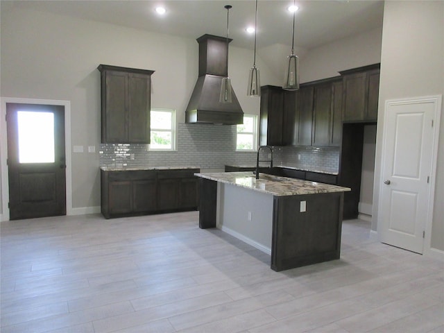 kitchen featuring exhaust hood, hanging light fixtures, sink, light stone countertops, and a kitchen island